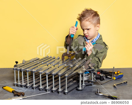 Cute little boy, child in image of auto mechanic or fitter in dungarees with work tools repairing auto motor isolated on yellow background. 86906050