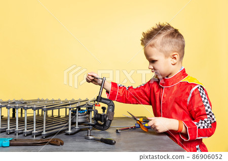 Cute little boy, child in image of auto mechanic or fitter in dungarees with work tools repairing auto motor isolated on yellow background. Cute little boy, child in image of auto mechanic or fitter in dungarees with work tools repairing auto motor isolated on yellow background. 86906052