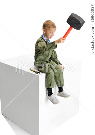 One little boy, cute kid in image of auto mechanic or fitter in green dungarees with work tools sitting on big box isolated over white studio background. One little boy, cute kid in image of auto mechanic or fitter in green dungarees with work tools sitting on big box isolated over white studio background. 86906057