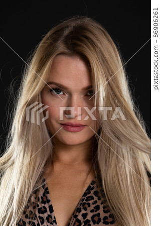 Close-up portrait of an attractive young blonde woman. Long hair. Black background. 86906261