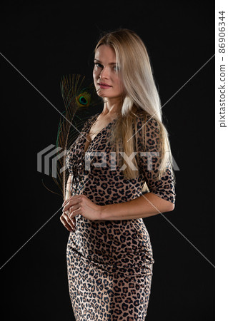 Young girl stands on black background and in her hands she holds peacock feather. She is blonde with long hair. Young girl stands on black background and in her hands she holds peacock feather. She is blonde with long hair. 86906344