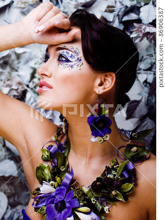 floral face art with anemone in jewelry, sensual young brunette woman in studio closeup 86906387