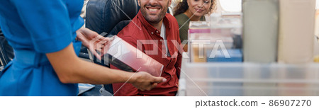 Smiling stewardess offering products or gifts to buy to passengers on aircraft. Air hostess walking with trolley with goods on aisle Smiling stewardess offering products or gifts to buy to passengers on aircraft. Air hostess walking with trolley with goods on aisle 86907270