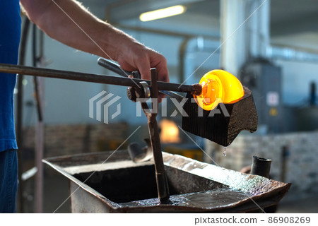Close-up of the hands of a master glassblower working with molten glass Traditional handmade crafts. Close-up of the hands of a master glassblower working with molten glass Traditional handmade crafts. 86908269