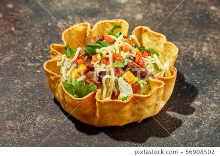 Taco salad in tortilla bowl with beef, cheese, corn and lettuce 86908502