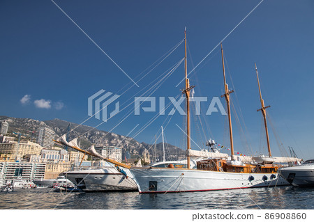 A lot of huge yachts are in port of Monaco at sunny day, Monte Carlo, mountain is on background, big masts of sail yacht, motorboat and mega yachts are moored in marina, sun reflection on glossy board A lot of huge yachts are in port of Monaco at sunny day, Monte Carlo, mountain is on background, big masts of sail yacht, motorboat and mega yachts are moored in marina, sun reflection on glossy board 86908860