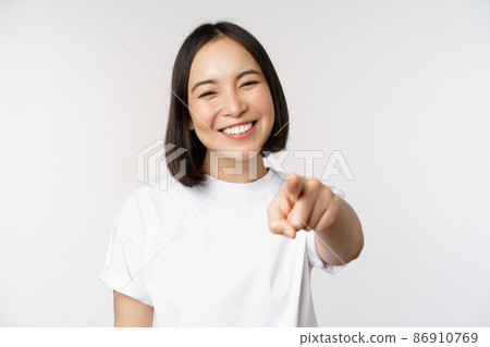 Portrait of happy smiling asian woman with white teeth, pointing finger at camera, choosing you, congratulating, standing over white background 86910769