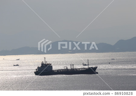 A landscape of land, mountains and sky with a dimly visible city and the sparkling sea surface where tankers and fishing boats come and go A landscape of land, mountains and sky with a dimly visible city and the sparkling sea surface where tankers and fishing boats come and go 86910828