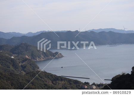A view of the sea of the blue bay with thin clouds, blue sky and harbor, peninsula, mountains, buildings and windmills for wind power generation A view of the sea of the blue bay with thin clouds, blue sky and harbor, peninsula, mountains, buildings and windmills for wind power generation 86910829