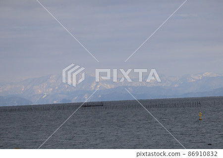 Scenery of Lake Biwa with snow-covered mountains, clouds, blue sky and aquaculture stakes Scenery of Lake Biwa with snow-covered mountains, clouds, blue sky and aquaculture stakes 86910832