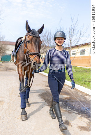 Young jockey teen girl walking with the horse before training 86911984