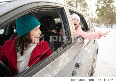 Happy family, mother and daughter in warm clothes travel by car on a beautiful cold snowy day. Adorable cheerful child, little girl catching snowflakes falling on her hand. Enjoy winter holiday Happy family, mother and daughter in warm clothes travel by car on a beautiful cold snowy day. Adorable cheerful child, little girl catching snowflakes falling on her hand. Enjoy winter holiday 86912426