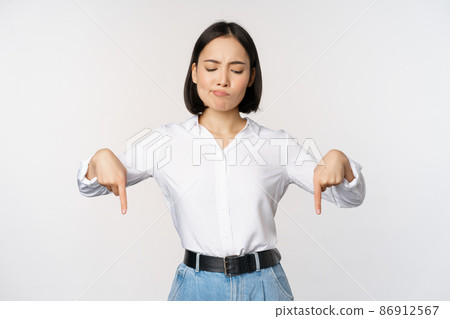 Portrait of skeptical, disappointed asian businesswoman, korean girl pointing and looking down with doubts, standing against white background Portrait of skeptical, disappointed asian businesswoman, korean girl pointing and looking down with doubts, standing against white background 86912567