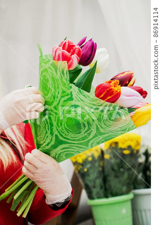 Woman florist makes bouquet of fresh tulips. Spring flowers in flower shop. Small business for gardeners. Growing plants in greenhouse. 86914114