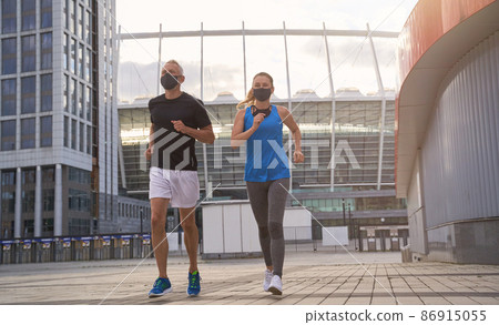 Full length shot of middle aged healthy couple in protective masks running together in the morning in the city 86915055