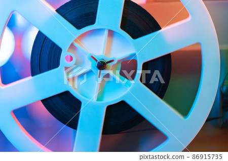 Retro reel with film rotating on sequins kinetic wall, colorful light. Old-fashioned 8mm projector 86915735