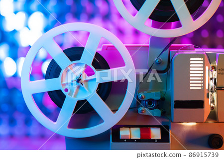 Retro reel with film rotating on sequins kinetic wall, colorful light. Old-fashioned 8mm projector 86915739