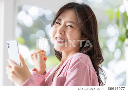 A woman in a room looking at the screen of a smartphone in a bright room A woman in a room looking at the screen of a smartphone in a bright room 86915977
