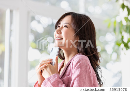 A woman in a room looking at the screen of a smartphone in a bright room A woman in a room looking at the screen of a smartphone in a bright room 86915978