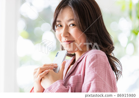 A woman in a room looking at the screen of a smartphone in a bright room 86915980