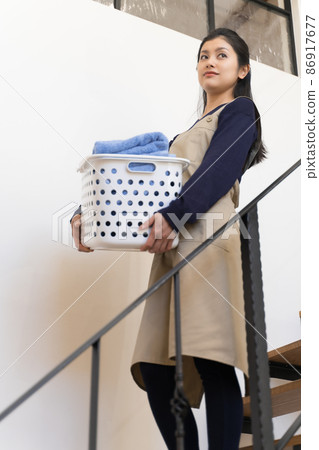 A young woman going down the stairs with a laundry basket (housekeeper, housekeeping agency, housekeeper) A young woman going down the stairs with a laundry basket (housekeeper, housekeeping agency, housekeeper) 86917677