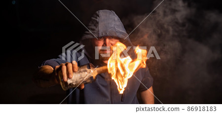 The man in the hood is holding a burning bottle. Molotov cocktail. 86918183