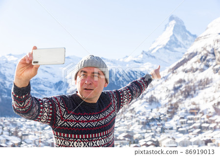 Travel blogger pointing at Matterhorn recording vlog with smartphone 86919013