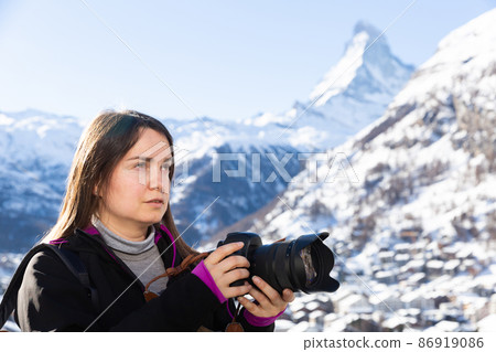Photographer woman with camera taking pictures of winter Swiss Alps 86919086