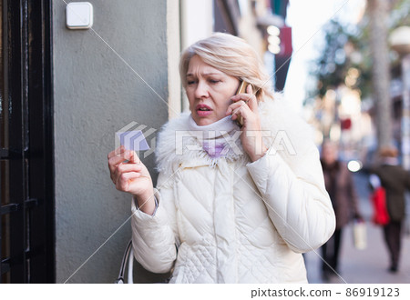 Female standing near door bell and holding phone and paper Female standing near door bell and holding phone and paper 86919123