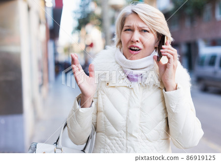 Adult female is talking by phone with friend on the street Adult female is talking by phone with friend on the street 86919125
