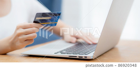 Hand of young woman holding credit card buying shopping online with laptop computer. 86920348