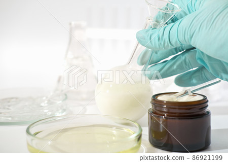 hand in rubber medical glove holding laboratory glassware with fermented cosmetic product, face cream with enzymes developed in a lab. hand in rubber medical glove holding laboratory glassware with fermented cosmetic product, face cream with enzymes developed in a lab. 86921199