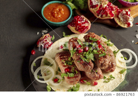 Sausages made of minced meat, on pita bread, with fresh herbs, onions, pomegranate seeds and hot tomato sauce. Close-up on a black background Sausages made of minced meat, on pita bread, with fresh herbs, onions, pomegranate seeds and hot tomato sauce. Close-up on a black background 86921763