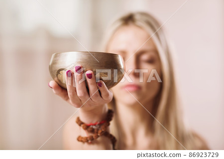 Blonde woman practicing yoga listens to the melody coming from the Tibetan bowl 86923729