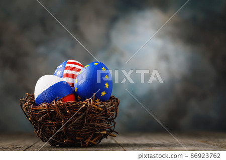 Three Easter eggs in a nest painted in colors of the flags of Russia, America and European Union on a wooden table with copy space Three Easter eggs in a nest painted in colors of the flags of Russia, America and European Union on a wooden table with copy space 86923762