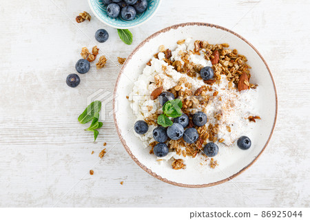 Bowl of granola with fresh blueberry, cottage cheese or curd, yogurt and nuts. Healthy food. Breakfast. Top view 86925044