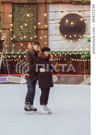 Young couple in love is skating, riding uncertainly, holding on to each other and laughing. Young couple in love is skating, riding uncertainly, holding on to each other and laughing. 86925239