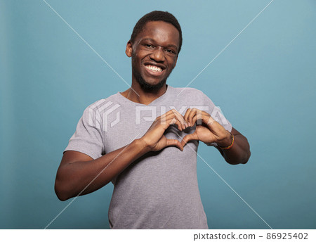 Young adult doing heart shaped sign with hands in studio Young adult doing heart shaped sign with hands in studio 86925402