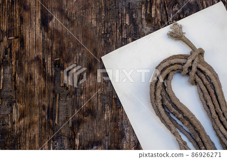 A roll of old rope and a white piece of paper on a dark wooden background. 86926271