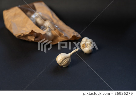 Brown paper bag with garlic against a black background. Heads of ripe garlic in the peel. Close-up. Selective focus Brown paper bag with garlic against a black background. Heads of ripe garlic in the peel. Close-up. Selective focus 86926279