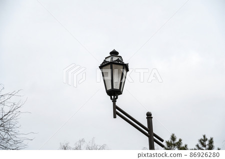 An antique-style street lamp against an overcast sky. It's cloudy. Daytime. An antique-style street lamp against an overcast sky. It's cloudy. Daytime. 86926280