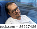 Tired millennial man in eyeglasses sitting near window in metro train in city. Mature exhausted male sleeping in subway after work. Tired gentleman taking a nap in public transport 86927486