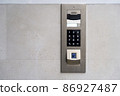 Matte metal intercom call panel with white digital buttons and fingerprint scanner on limestone wall of luxury residential house 86927487