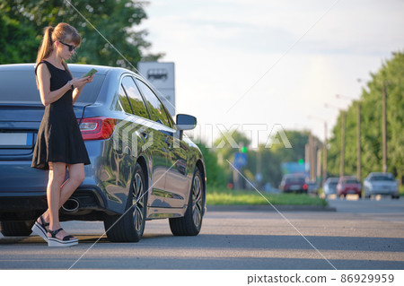 Young female driver standing near her car talking on mobile phone on a city street in summer 86929959