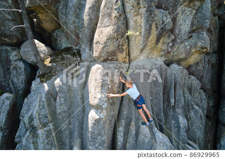 Young child boy climbing steep wall of rocky mountain. Kid climber overcomes challenging route. Engaging in extreme sport concept. 86929965