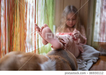 little cute girl plays a game console sitting on the windowsill 86930112