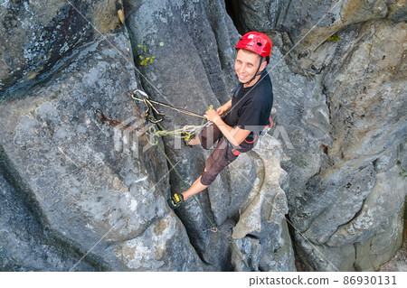 Strong male climber climbing steep wall of rocky mountain. Sportsman overcoming difficult route. Engaging in extreme sports hobby concept. 86930131