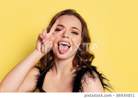 Studio shot of young pretty girl with long curly hair wearing black evening dress isolated on yellow background. Concept of emotions, beauty, fashion Studio shot of young pretty girl with long curly hair wearing black evening dress isolated on yellow background. Concept of emotions, beauty, fashion 86930851