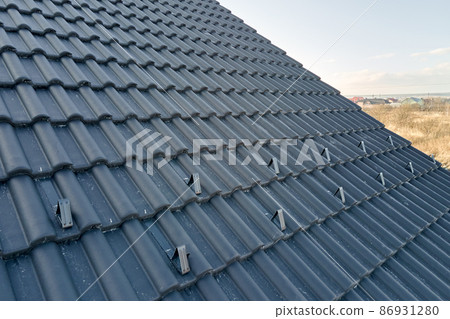 Closeup snow guard for safety in winter on house roof top covered with ceramic shingles. Tiled covering of building Closeup snow guard for safety in winter on house roof top covered with ceramic shingles. Tiled covering of building 86931280
