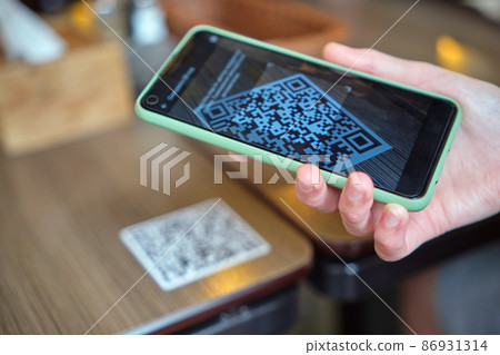 Closeup of guest hand ordering meal in restaurant while scanning qr code with mobile phone for online menu. Closeup of guest hand ordering meal in restaurant while scanning qr code with mobile phone for online menu. 86931314